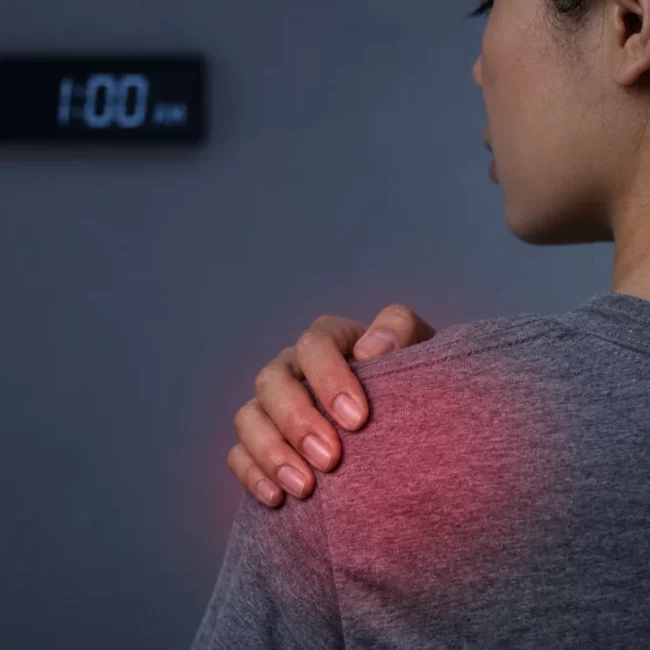 Woman experiencing shoulder pain while touching the affected shoulder at night